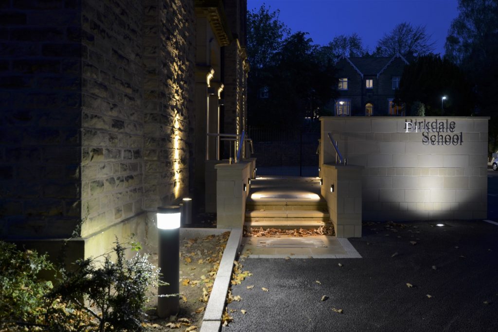 Raised stainless steel lettering on the ashlar sandstone picked out with a ground recessed spotlight.